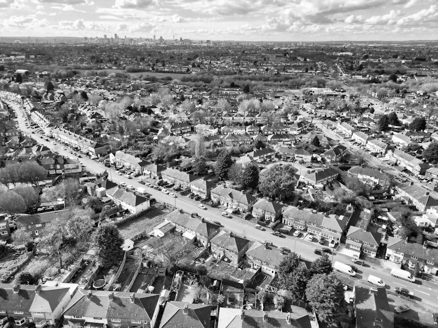 A residential street scene showing a row of parked cars and vans on both sides of the road, with some Vans, associated with Man with Van Enfield, visible near the curb. The street is lined with terrac